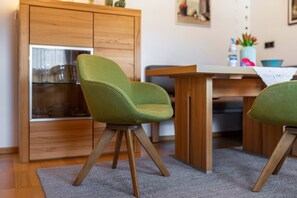 Una habitación con un armario de madera, una mesa y dos sillas verdes con patas de madera.