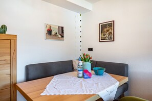A dining area with a table, chairs, a vase with flowers, a bottle, and two framed pictures on the wall.