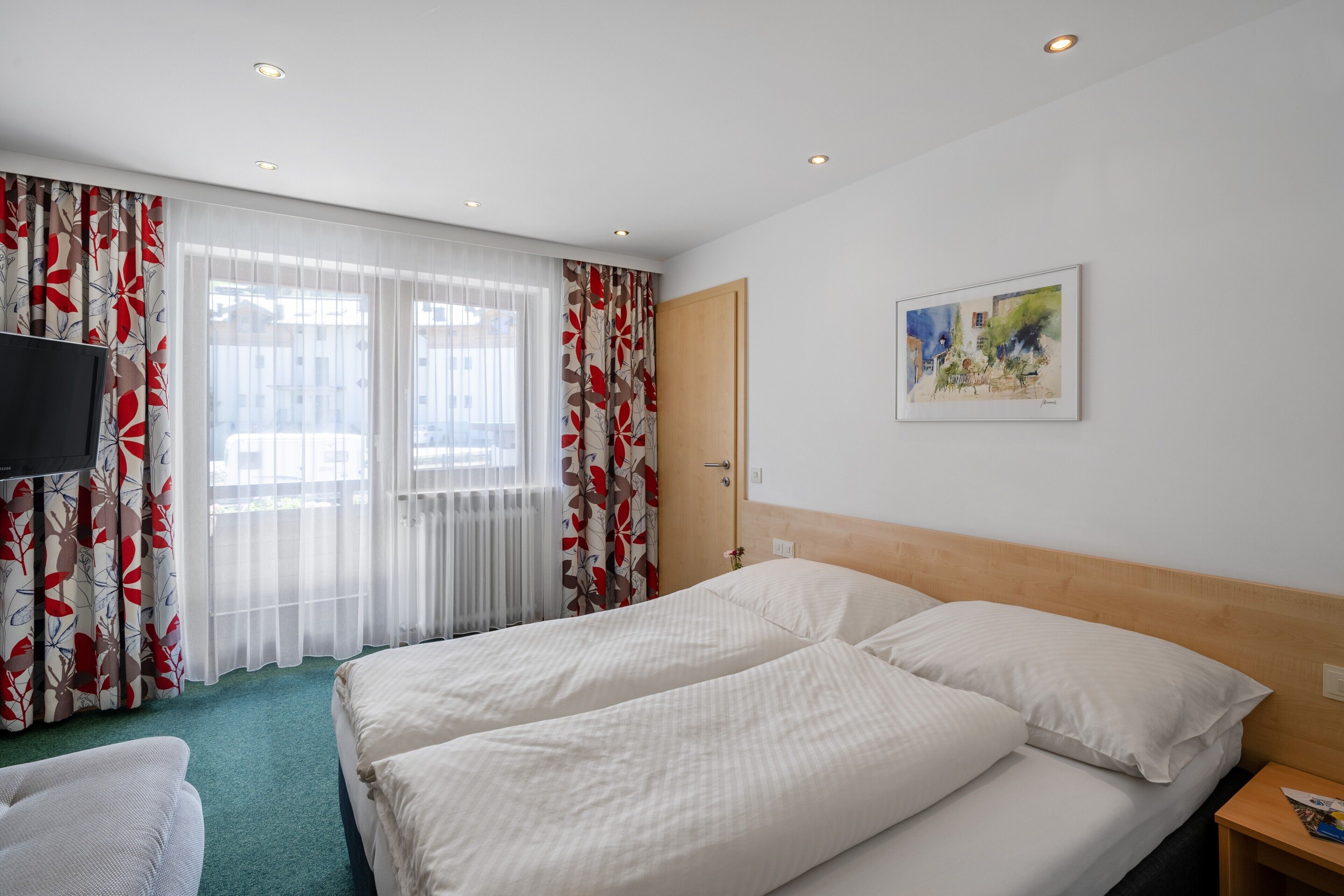 Habitación de hotel con dos camas, televisión, un cuadro en la pared y ventana con cortinas.