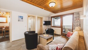 Un salon avec un plafond en bois, un téléviseur, un canapé, une table basse et un coin repas.