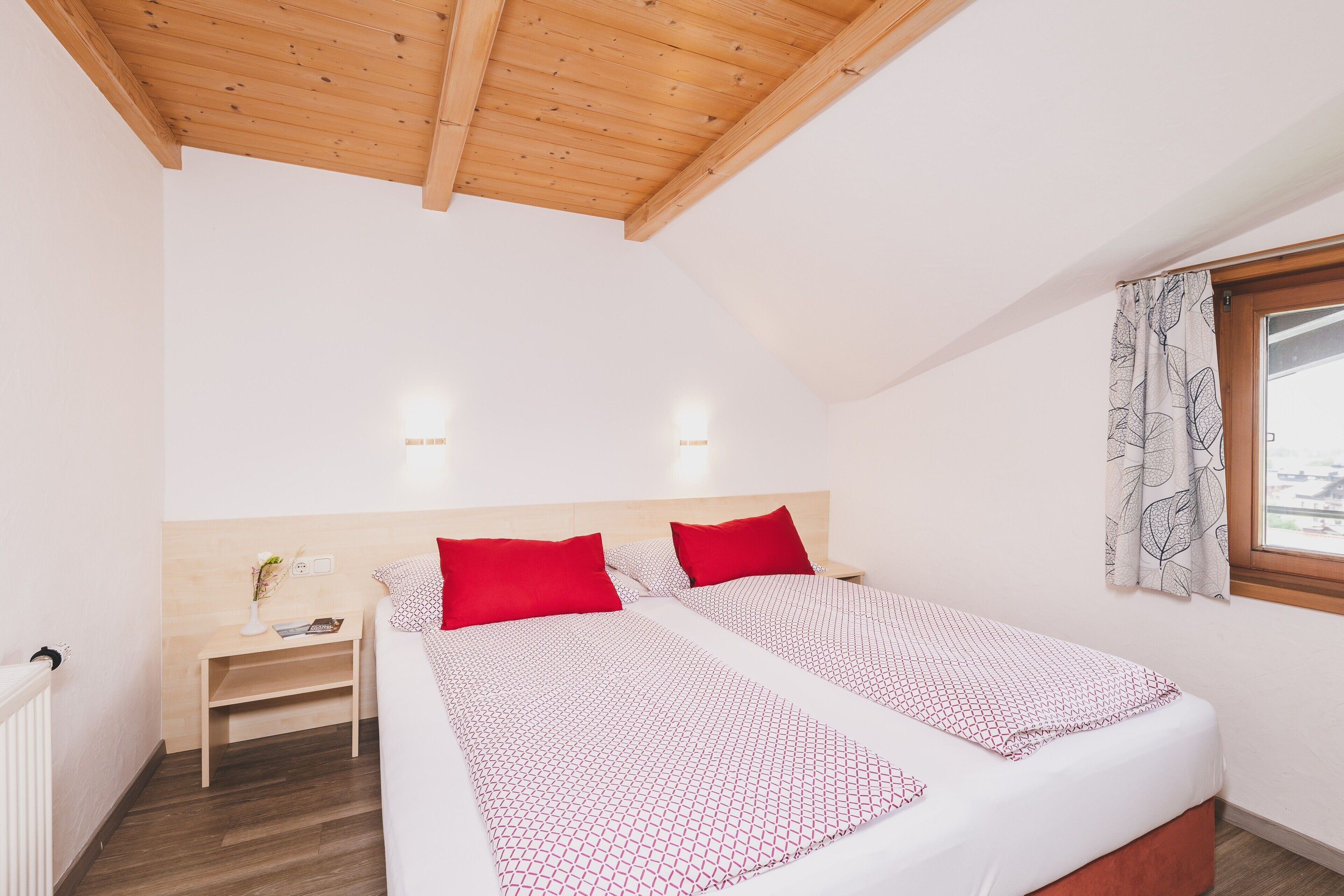Un dormitorio con dos camas, vigas de madera en el techo, mesitas de noche y una ventana con cortinas.