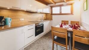 Une cuisine compacte avec des meubles blancs, un plan de travail en bois, un four encastré et un coin repas avec une table dressée pour deux personnes.