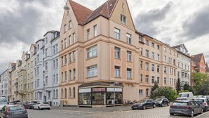 A multi-story building with a corner entrance, a ground-floor shop, and parked cars.