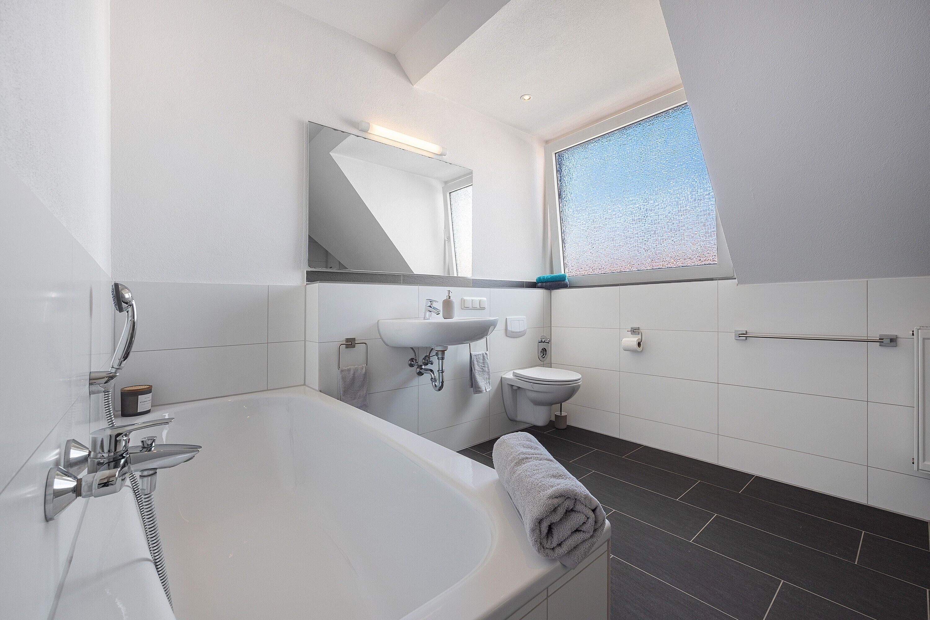 A modern bathroom with a bathtub, a sink, a toilet, and a large mirror.