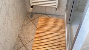 A bathroom with a white tiled wall, a white radiator, and a wooden slatted shower mat.