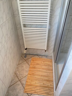 A bathroom with a white tiled wall, a white radiator, and a wooden slatted shower mat. - Apartment 'Haus Cürsgen - Ferienwohnung Jana' with Wi-Fi (Berlin)
