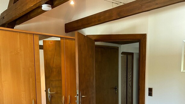 A bedroom with a wooden bed frame, a wardrobe, and a door leading to another room.