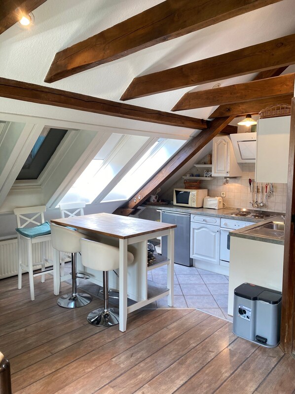 A kitchen with a wooden beam ceiling, white cabinets, a dining table with chairs, and a trash bin.