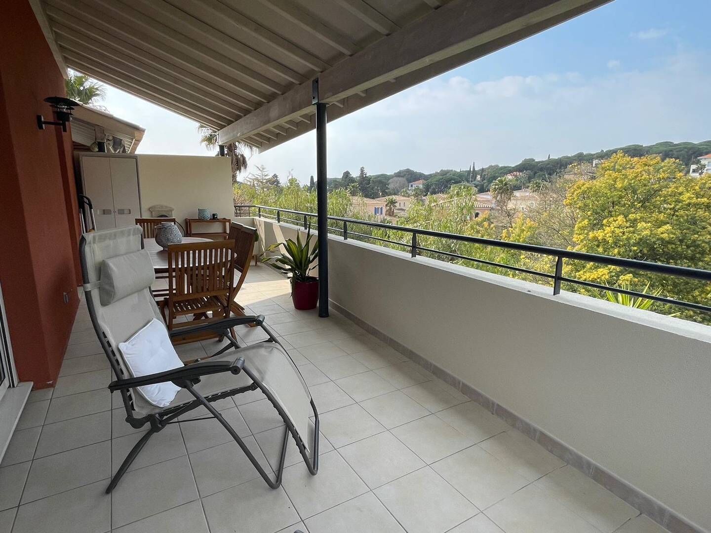 A balcony with a view of a town, a chair, a table, and a potted plant.