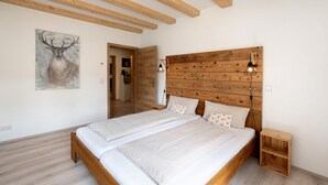 A bedroom with a wooden headboard, two beds, a nightstand, a wall-mounted lamp, and a painting of a deer.