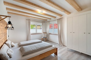 Ein Schlafzimmer mit einem Holzbett, einem Kleiderschrank, einem Stuhl und einem Fenster mit Vorhängen.