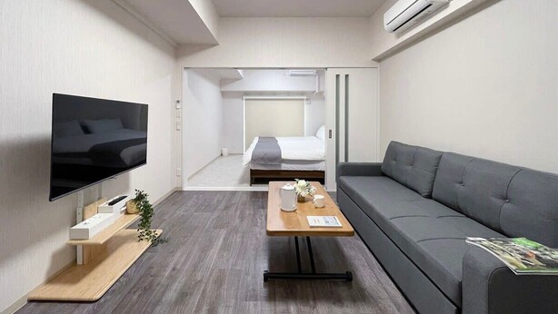 A modern hotel room with a flat-screen TV, a sofa, a wooden coffee table, and a bed in the background.