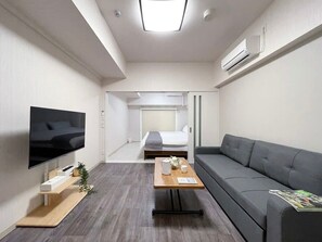 Una habitación de hotel moderna con una televisión de pantalla plana, un sofá, una mesa de centro de madera y una cama al fondo.