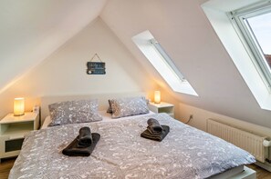 A bedroom with a sloped ceiling, two bedside tables with lamps, a bed with patterned bedding, and a skylight.