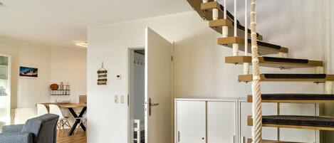 Eine Treppe mit Seilgeländer, einem weißen Schrank und einem Essbereich mit Stühlen und Tisch.