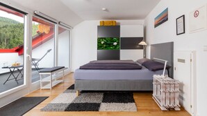 Een slaapkamer met een bed, een bureau, een stoel, een raam en uitzicht op een balkon.