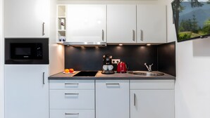Een moderne keuken met witte kastjes, een zwarte magnetron, een rode koffiezetapparaat en een spoelbak.