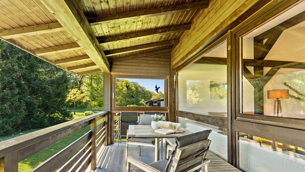 Eine Holzterrasse mit Tisch und Stühlen, mit Blick auf eine bewaldete Landschaft.