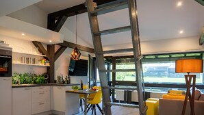 Ein modernes Interieur mit einem Schlafplatz im Loft-Stil, einer Küche mit Einbauofen, einem Essbereich und Blick durch große Fenster.