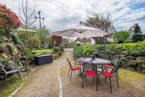 An outdoor patio with a table and chairs, surrounded by greenery and a stone pathway.
