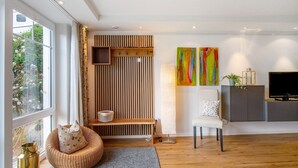 Ein modernes Wohnzimmer mit großem Fenster, einer Holzbank, einem weißen Sessel, einem Fernseher und einem Schrank.