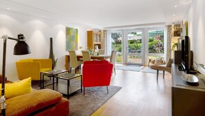 Ein modernes Wohnzimmer mit Sofa, Sesseln, Couchtisch, Fernseher und Essbereich mit Tisch und Stühlen.