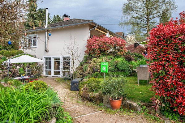 A house with a garden, a patio with outdoor furniture, and a sign indicating a garden area.