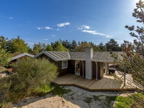 Una casa moderna con techo inclinado, terraza de madera y un ventanal grande.