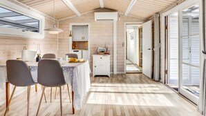 Een ruime kamer met een houten plafond, een eethoek met een tafel en stoelen, een keuken met kastjes en een grote schuifpui naar buiten.