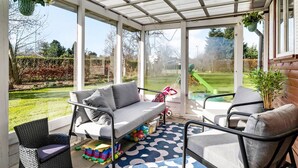 Een overdekt terras met een bank, stoelen en een speelruimte met speelgoed.