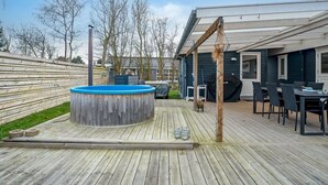 Een houten terras met een jacuzzi, zitplaatsen buiten en een overdekte patio.