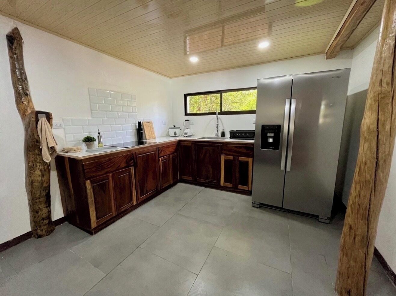 A kitchen with wooden cabinets, a stainless steel refrigerator, and a window providing natural light.
