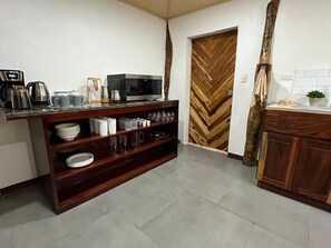 Una cocina con microondas, hervidor y diferentes vajillas en estantes.