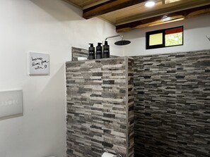 Un baño con paredes de textura de piedra, ducha con cabezal de ducha manual y un cartel con un mensaje positivo.