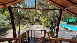 Eine Holzterrasse führt zu einem Poolbereich mit Blick auf einen Garten und Bäume.