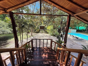 A wooden deck leading to a pool area with a view of a garden and trees.