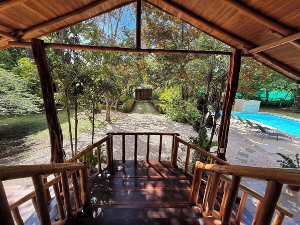 Una terraza de madera que conduce a un área de piscina con vistas a un jardín y árboles.