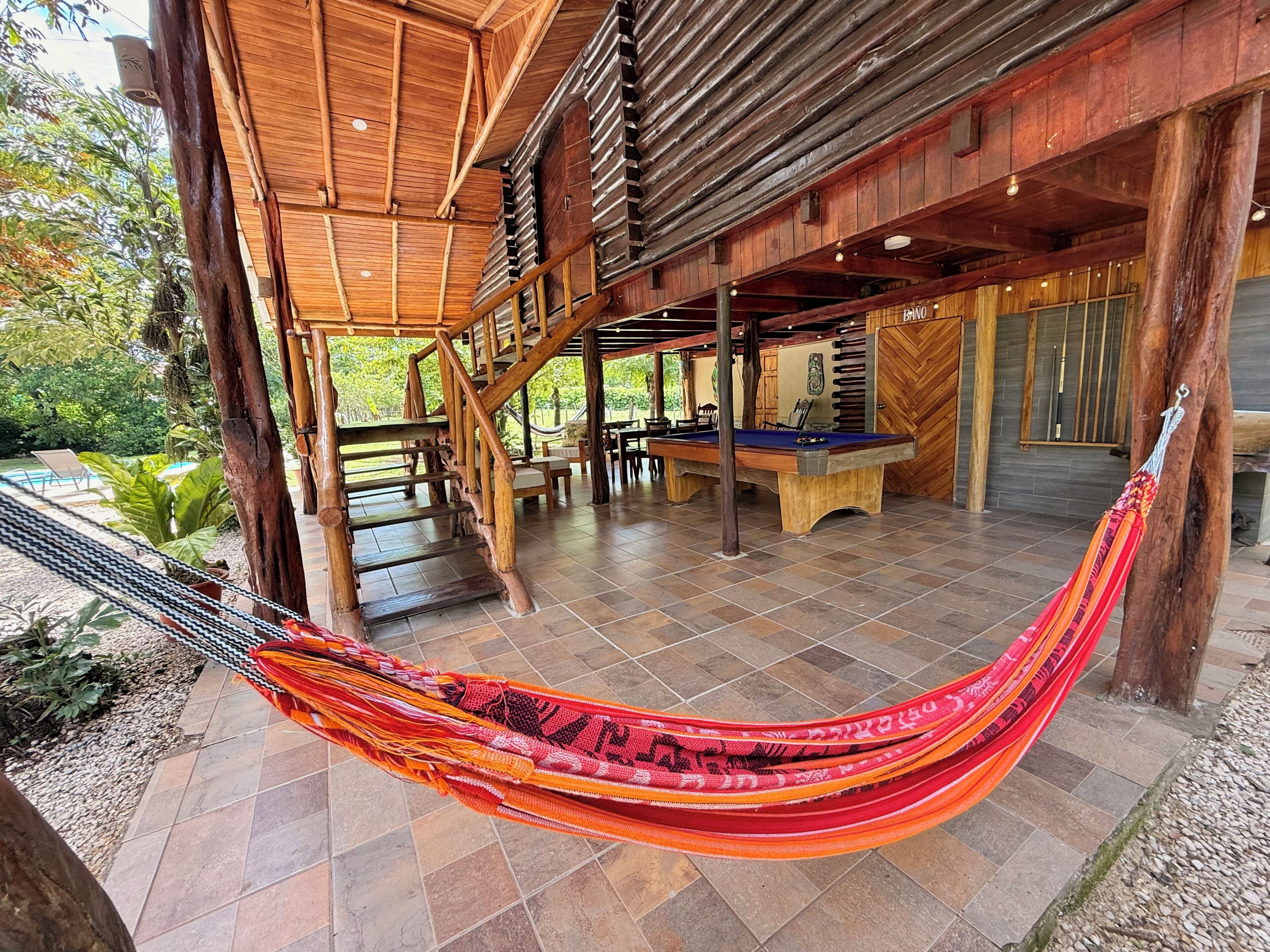 A wooden outdoor area with a pool table, a hammock, and a staircase.