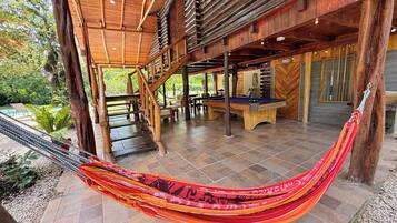 A wooden outdoor area with a pool table, a hammock, and a staircase.