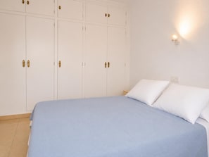 A bedroom with a bed, white walls, and a wardrobe with multiple doors.