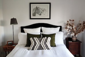 A neatly made bed with white and green pillows, a framed horse picture on the wall, a lamp, and a nightstand with a vase of dried flowers. - The Homestead -Discover Your Perfect Rural Retreat (Woodstock)