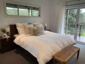 Ein Schlafzimmer mit einem großen Bett, einem Nachttisch mit Lampe, einer Bank und einem Fenster mit Blick auf Grünflächen.