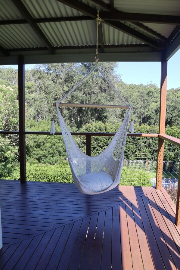 Una silla colgante en una terraza de madera con vistas a un área boscosa.