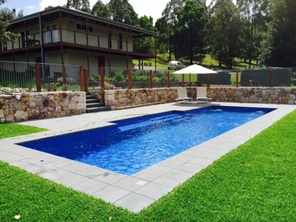 A rectangular swimming pool with a stone border, surrounded by a well-maintained lawn and a house in the background. - The Homestead -Discover Your Perfect Rural Retreat (Woodstock)
