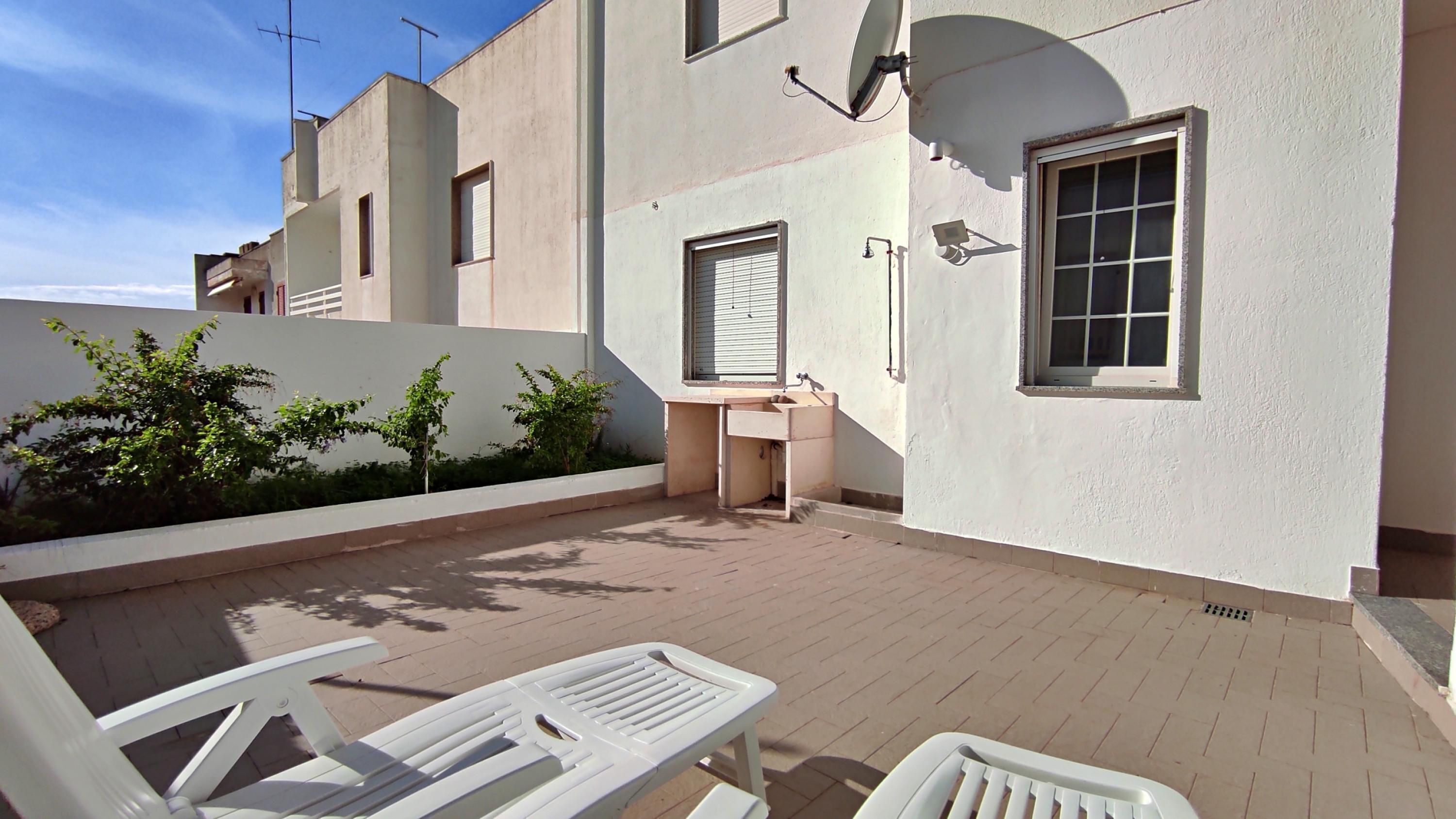 A small outdoor area with a white bench, a sink, and a window.