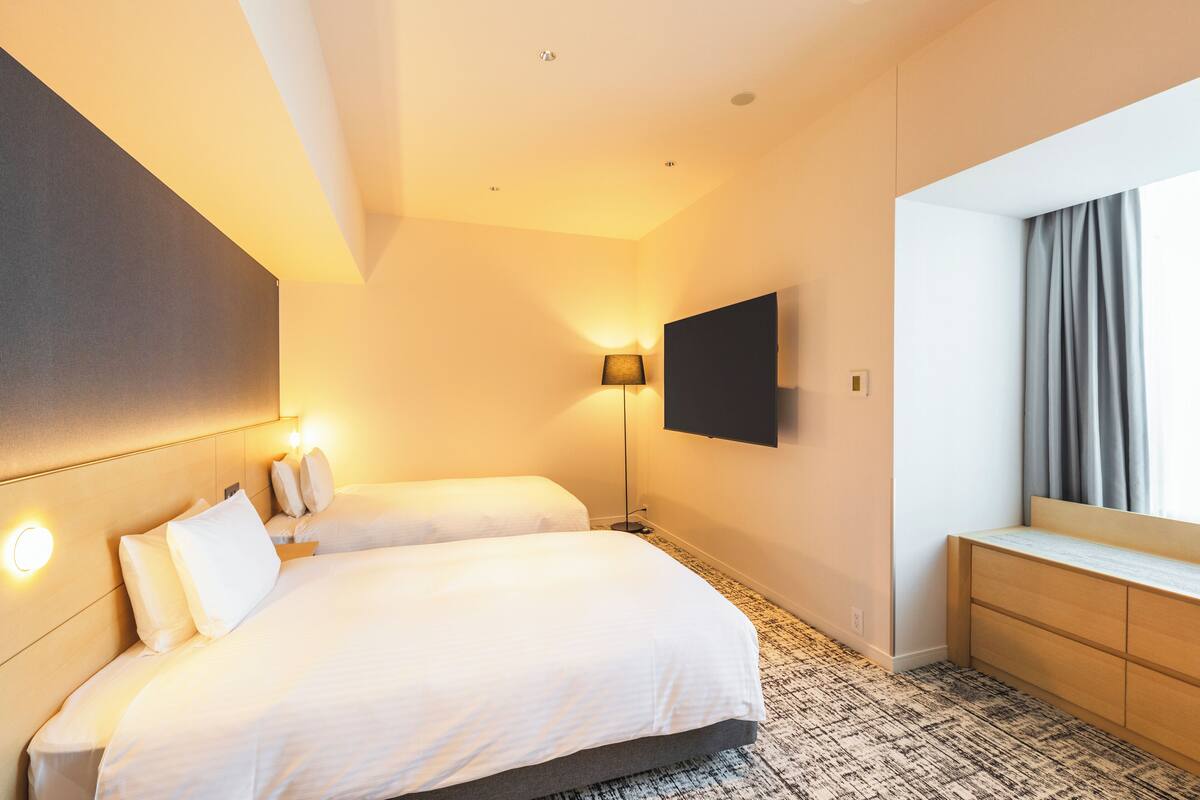 Habitación de hotel con dos camas, un televisor de pantalla plana, un escritorio y una ventana con cortinas.