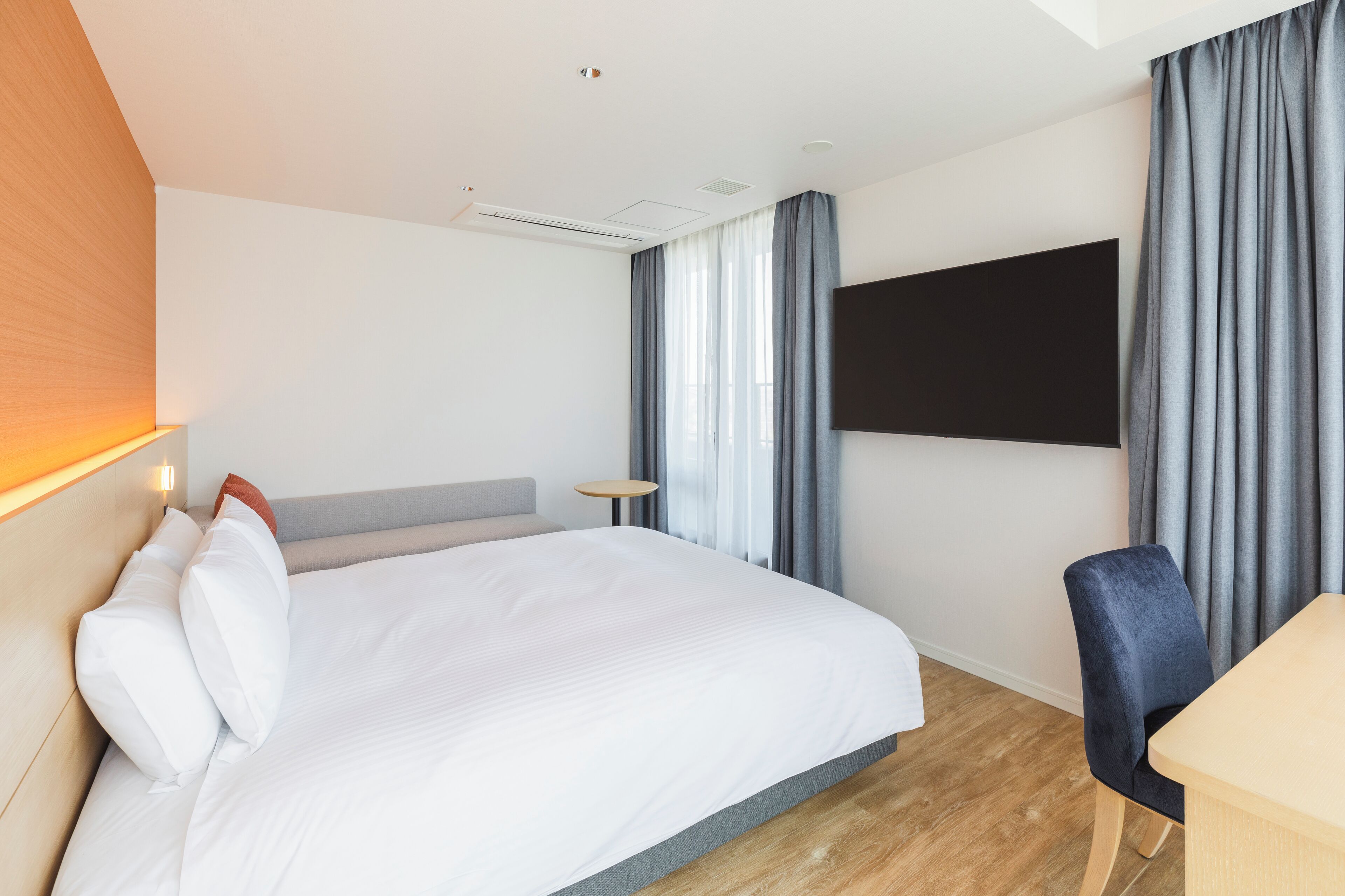 Hotellihuone, jossa on sänky, työpöytä, tuoli, televisio ja ikkuna, jossa on verhot.