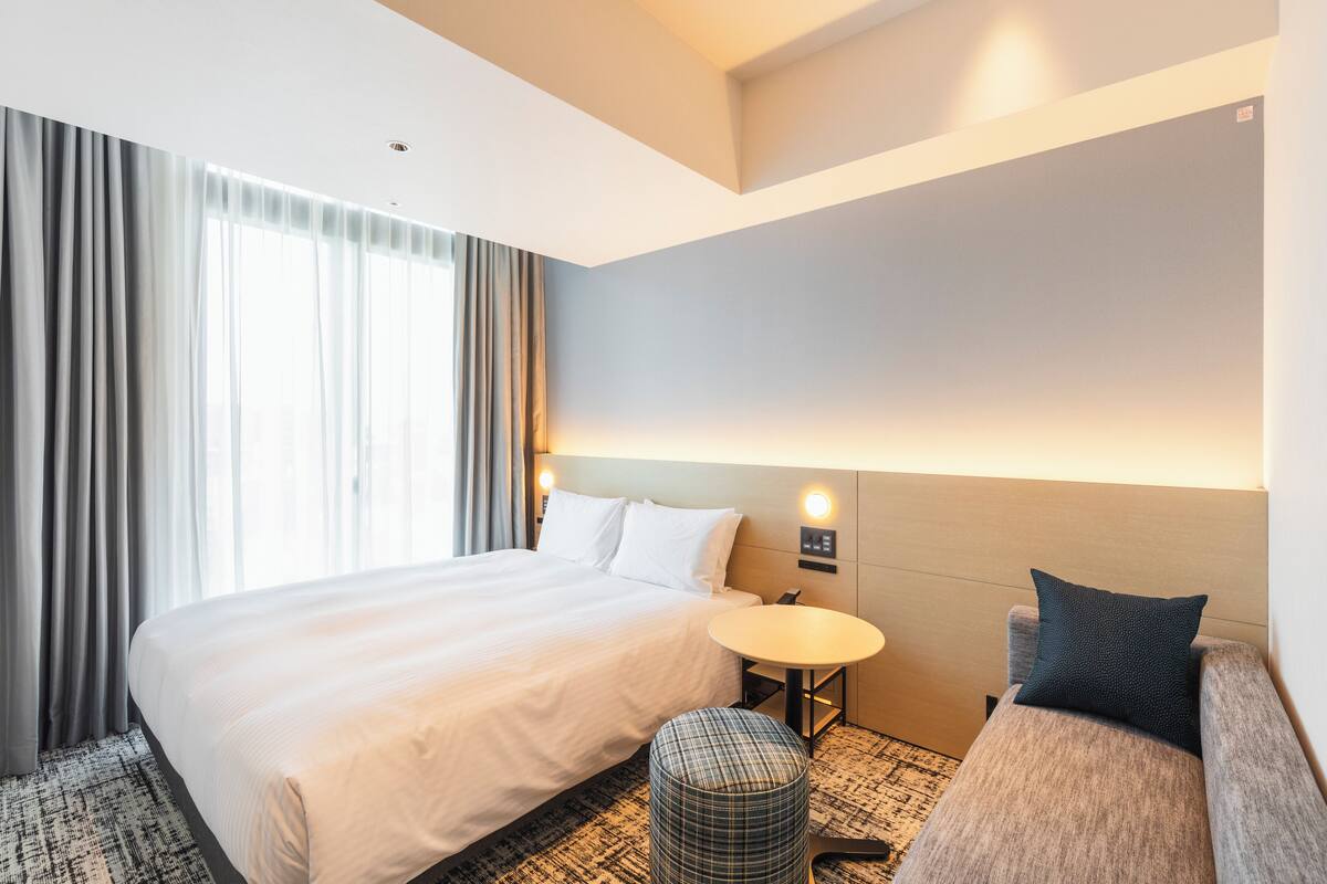 Una habitación de hotel con una cama grande, una mesita redonda pequeña, un sofá y una alfombra estampada.
