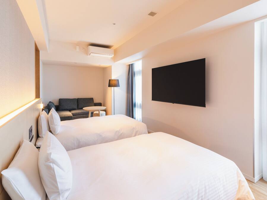 A hotel room with two beds, a flat-screen TV mounted on the wall, a desk, and a sofa.