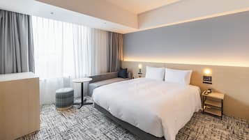 A hotel room with a large bed, a small round table, a sofa, and a nightstand with a lamp.